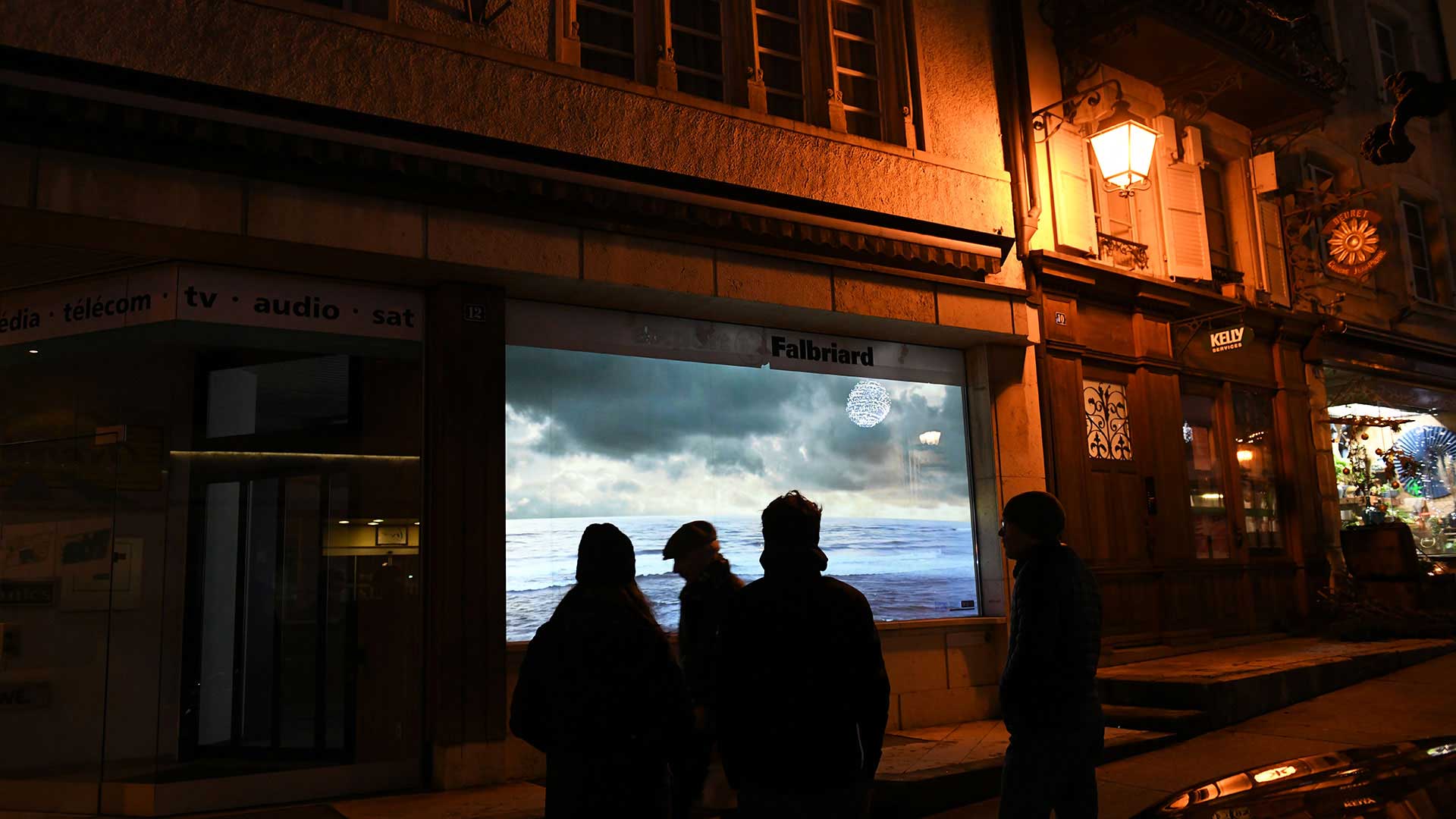 Trois passants devant une vitrine animée par une projection de paysages "infinite landscape"
